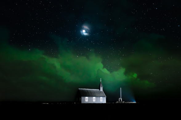 L'ovale auroral nimbe les nuages au dessus de l'église de Budir d'une couleur verte en ce soir d'éclipse lunaire, Islande