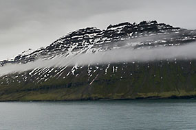 Arrivée dans le Seydisfjordur, les nuages flottent le long des falaises encore enneigées.
