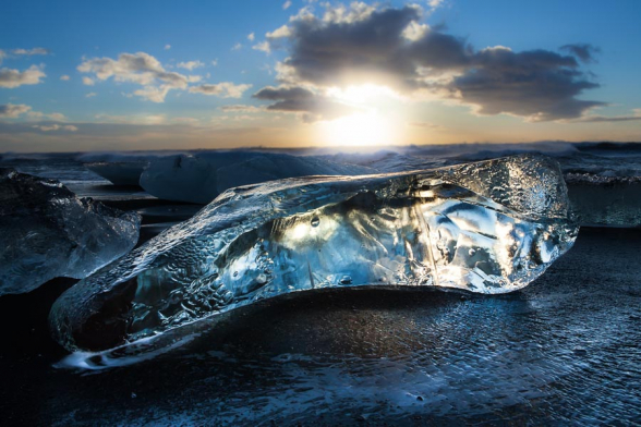 Le soleil levant révèle la transparence de ce gros glaçon, ancien iceberg, échoué sur la plage de sable noir de la lagune glaciaire de Jokulsarlon, Islande
