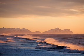 Le lever du soleil éclaire l'écume des vagues qui déferlent sur la plage de sable noir de la lagune galcière du Jokulsarlon