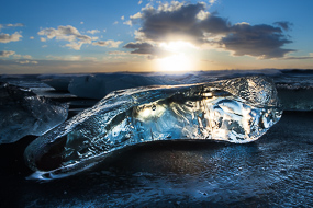 Le soleil levant révèle la transparence de ce gros glaçon, ancien iceberg, échoué sur la plage de sable noir de la lagune glaciaire de Jokulsarlon, Islande