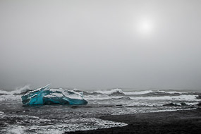 Iceberg échoué sur la plage de sable noir et battu par les vagues, en face de la lagune glaciaire du Jokulsarlon, Islande
