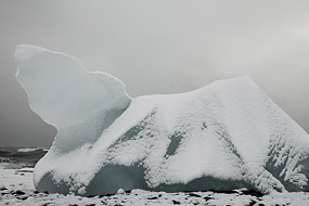 Iceberg échoué sur la plage de sable noir, recouvert de neige,  en face de la lagune glaciaire du Jokulsarlon, Islande