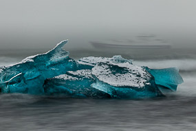 Le bateau fantôme. « A tribute to the Titanic ». Un bateau passe au large, dans le brouillard, pas très loin des icebergs échoués sur la plage en face du Jokulsarlon, Islande.
