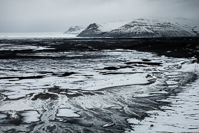 Le torrent Skeidara se transforme en sandur, il charrie les alluvions glaciaires  jusqu'à la mer et forme ce paysage monochrome, le sable noir étant recouvert par la neige, sud de l'Islande
